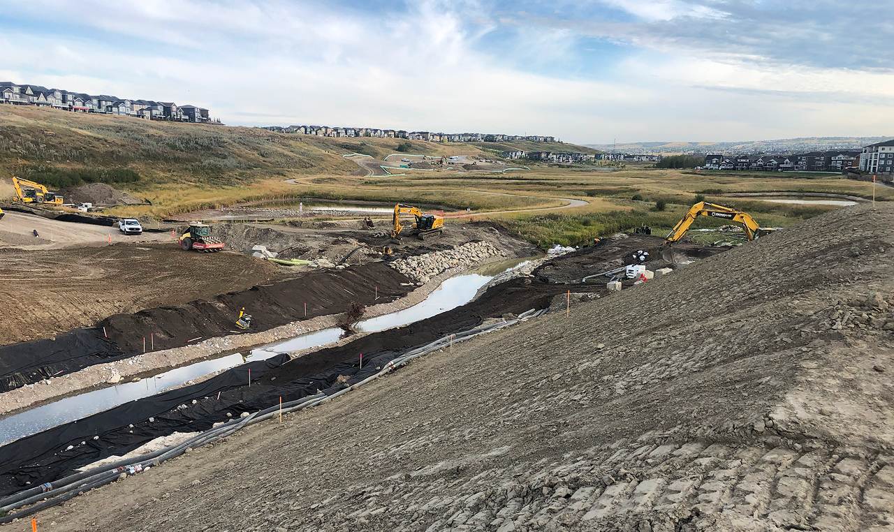 Multiple excavators shaping West Nose Creek realignment channel with erosion control geotextile installation