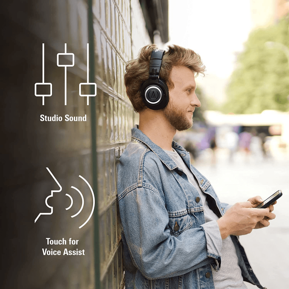 Man wearing Audio-Technica ATH-M50xBT wireless headphones, using a smartphone. Features studio-quality sound and voice assistant control