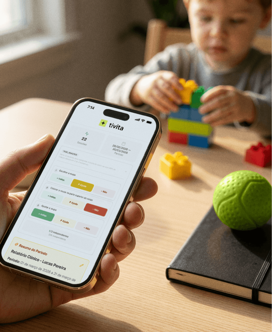 Mão segura um celular exibindo a tela do aplicativo da Tivita com o relatório clínico de uma sessão de terapia, mostrando 22 sessões no período e marcações de desempenho por cores (verde, amarelo e vermelho), enquanto ao fundo uma criança brinca com blocos de montar sobre a mesa, ilustrando o registro de dados de sessão usado por clínicas de terapia ABA na Tivita.
