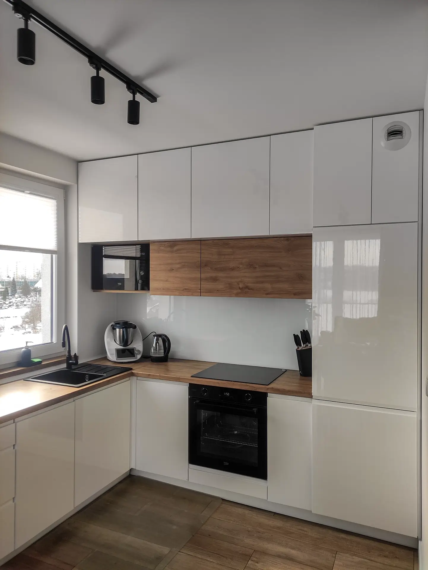 Minimalistyczna biała kuchnia z drewnianym akcentem – projekt i montaż mebli Kraków.