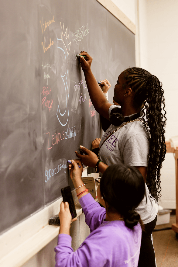 Highschool student writing her name with an affirmation on a chalkboard at Sewanee Univeristy. 