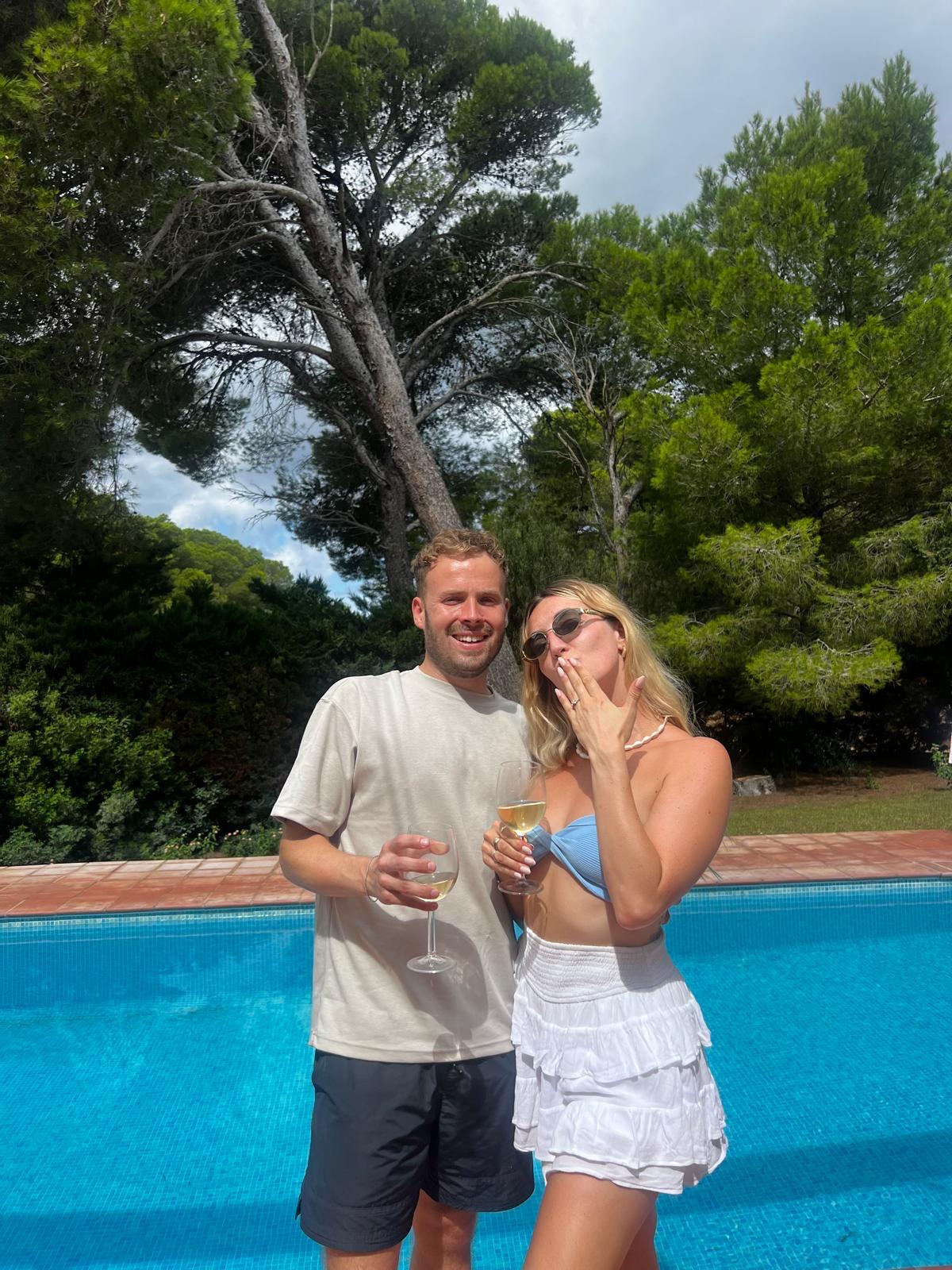 Close-up of two hands gently clasped, one wearing a sparkling engagement ring. The soft lighting and pastel nails evoke a sense of romance and intimacy.