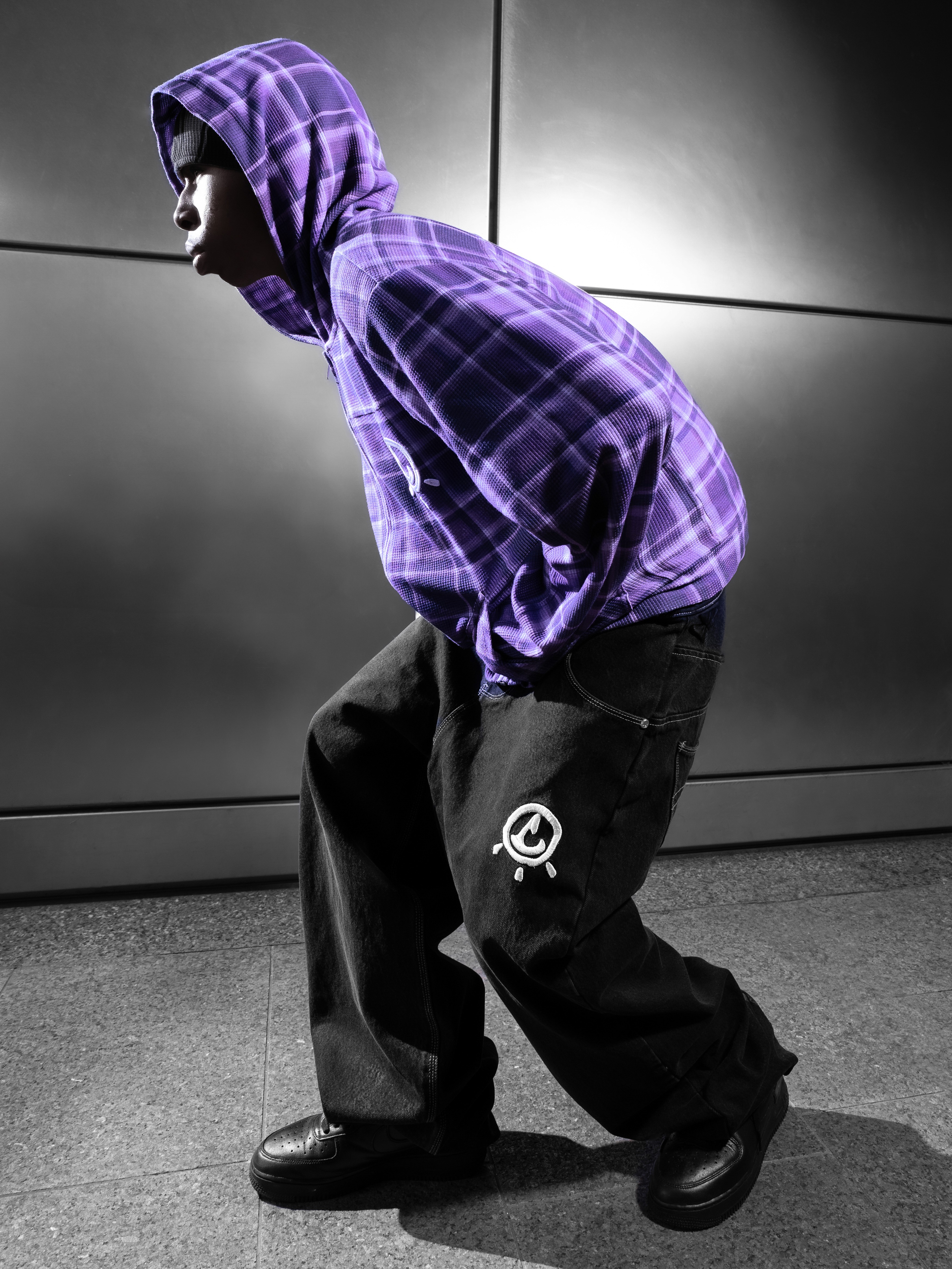 Smiling man in a white hoodie and black pants standing confidently on a bright green football field with empty stadium seats behind.