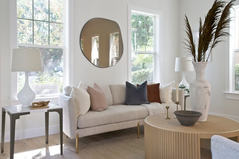Serene living room with a beige sofa, round mirror, and natural light in Bonita Canyon Remodel.