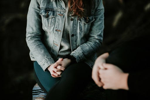 Photo of two people sitting near each other, one in center and one out of focus to the right