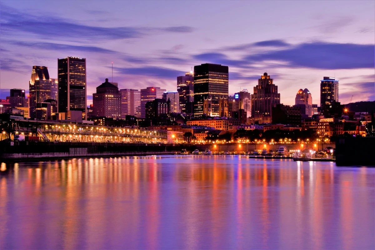 Montreal skyline at sunset with city lights reflecting on the St. Lawrence River.
