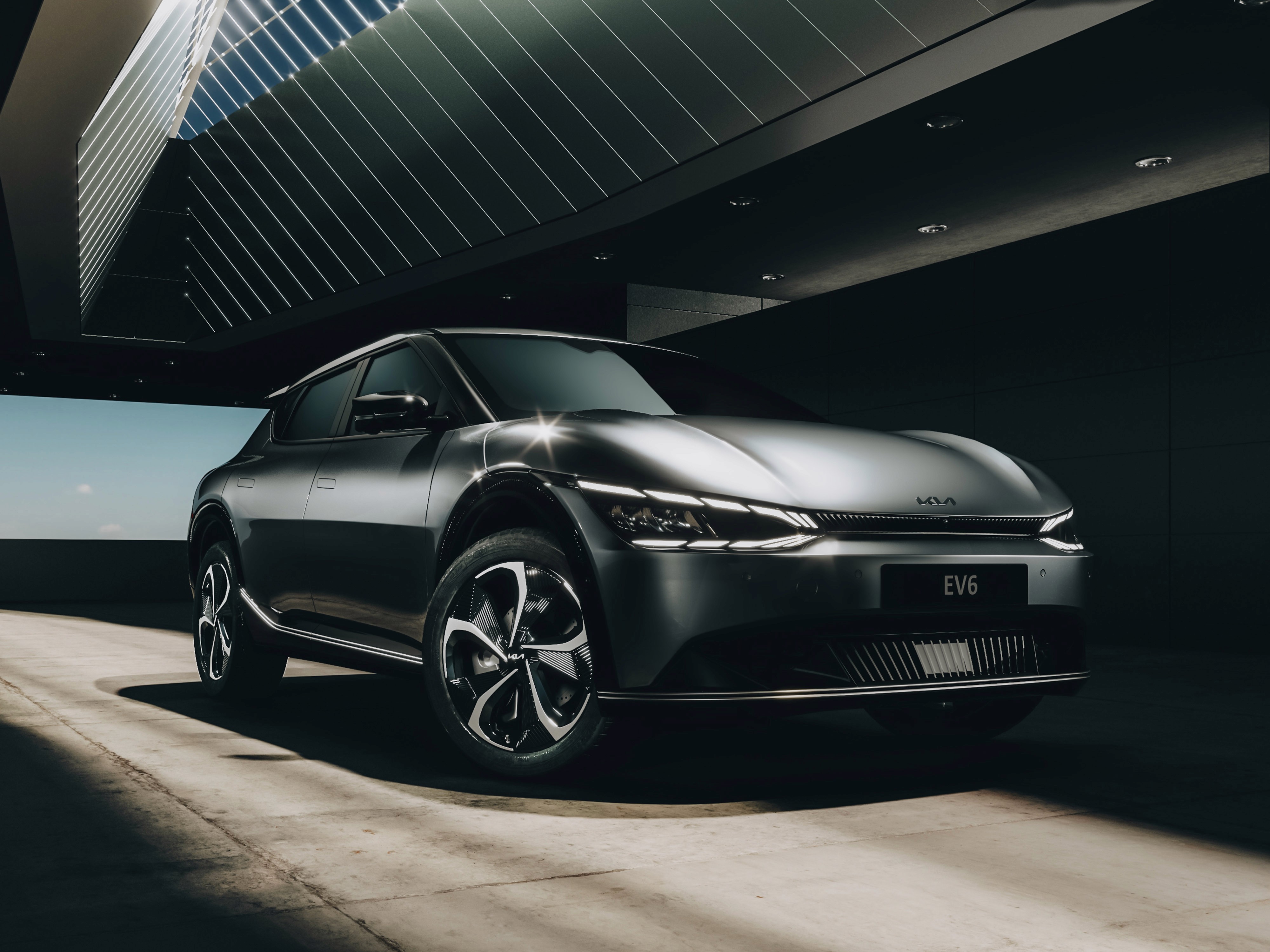 Render vista tre quarti frontale di Kia EV6 in ambiente architettonico moderno e minimalista in stile advertising.