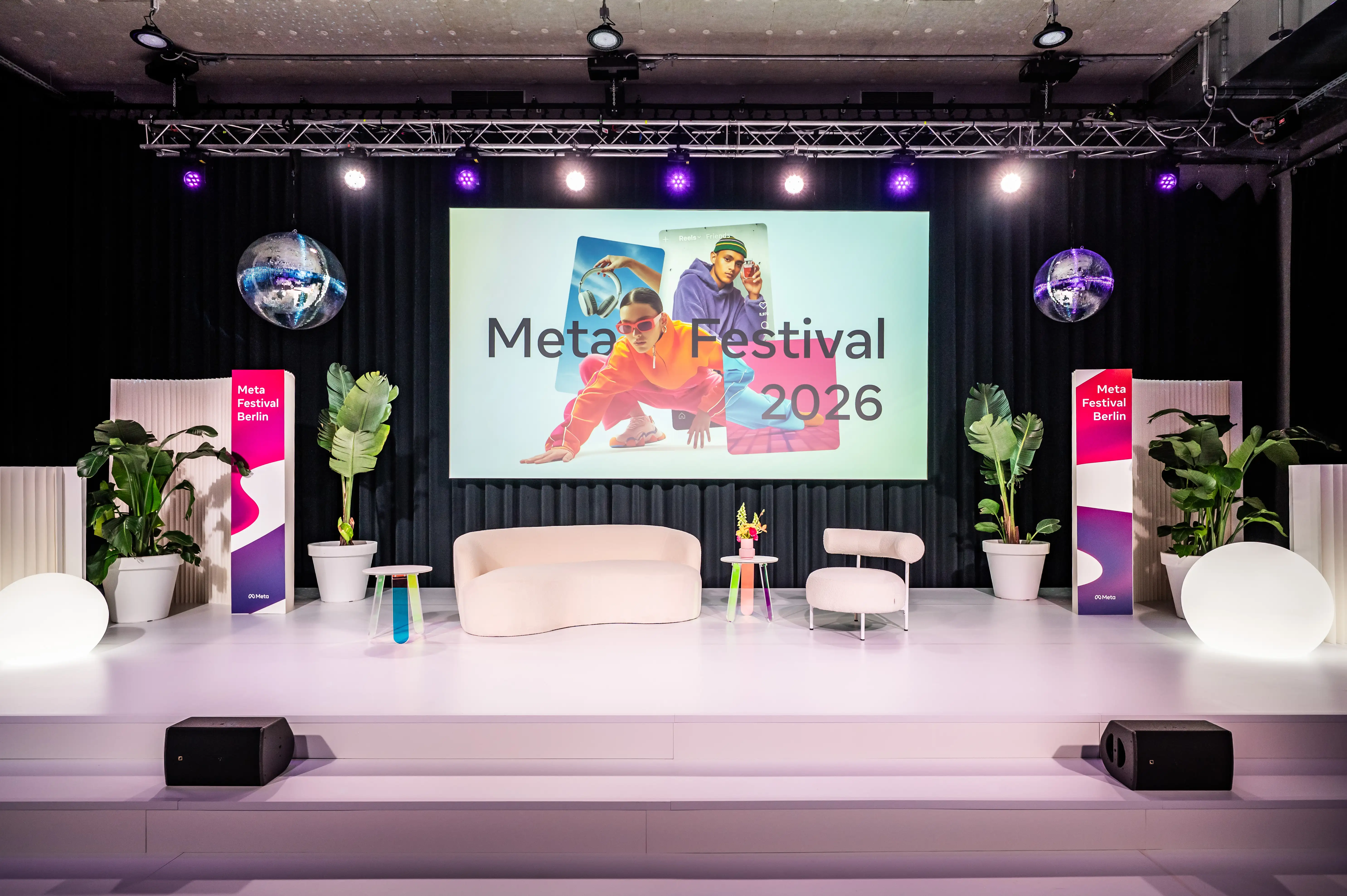 White stage with cream sofa, armchair, plants and Meta Festival 2026 screen between banner pillars.