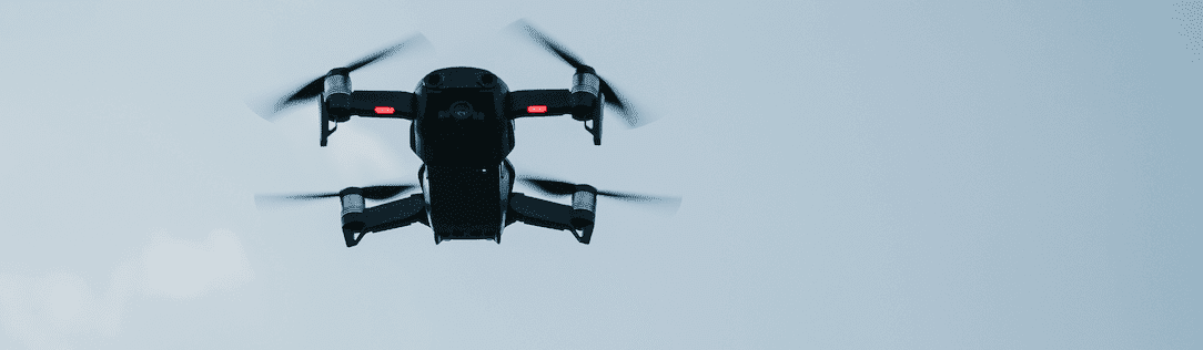 Black quadcopter drone flying against a pale grey sky