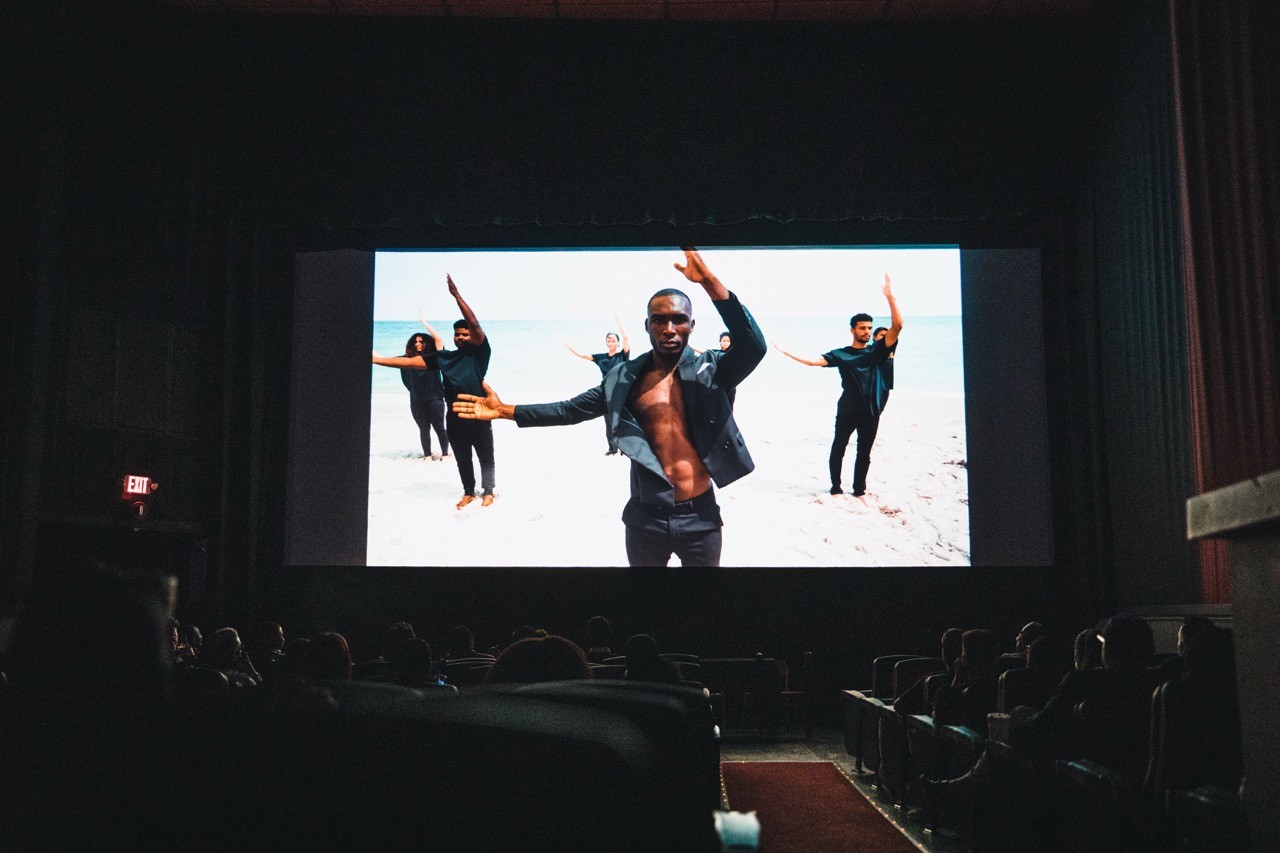 Photo of a movie screen in a theater showing a performance shot, Benjamin Jean screening moment.