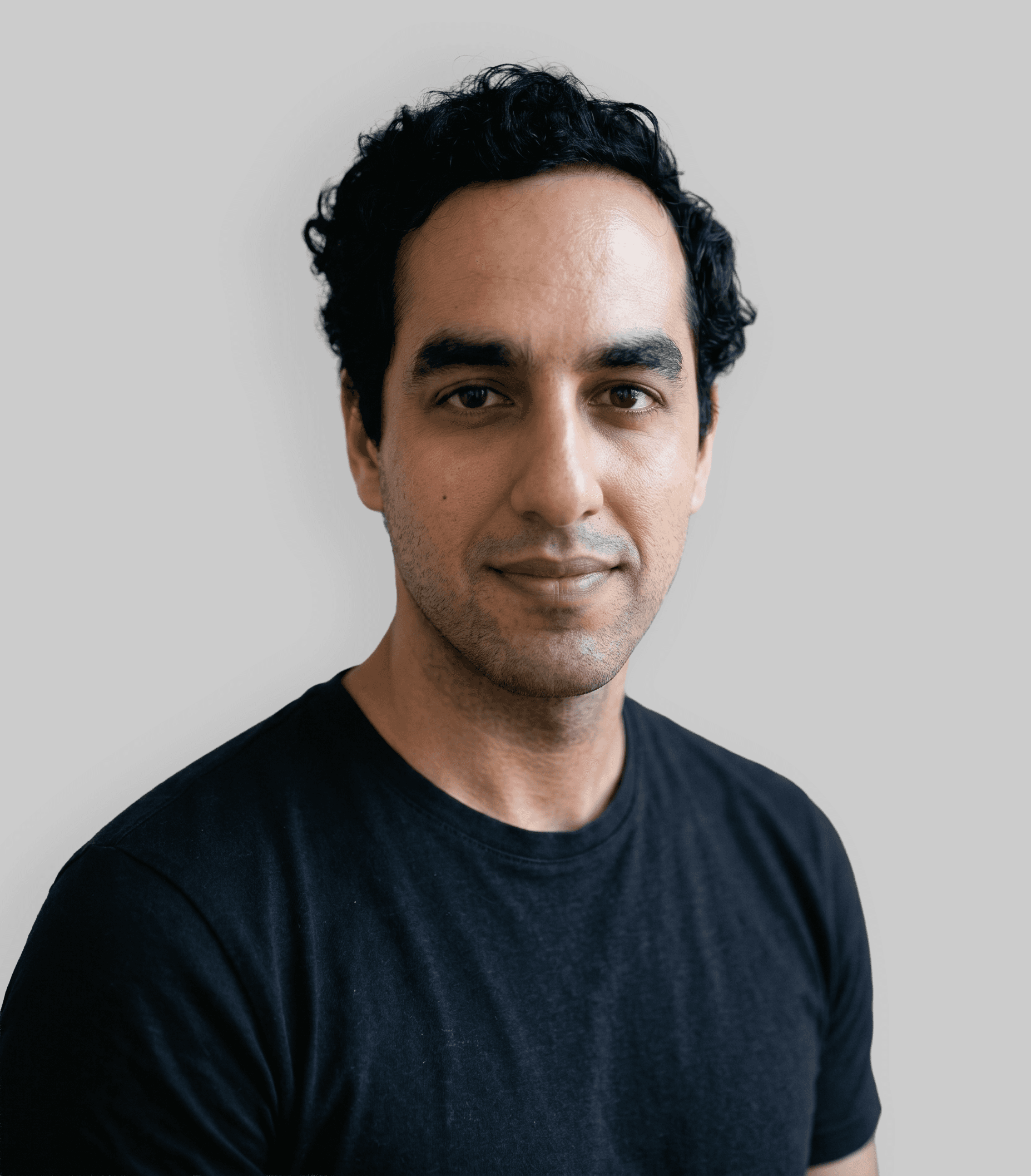 A smiling individual with curly hair and a green shirt, against a light gray background.