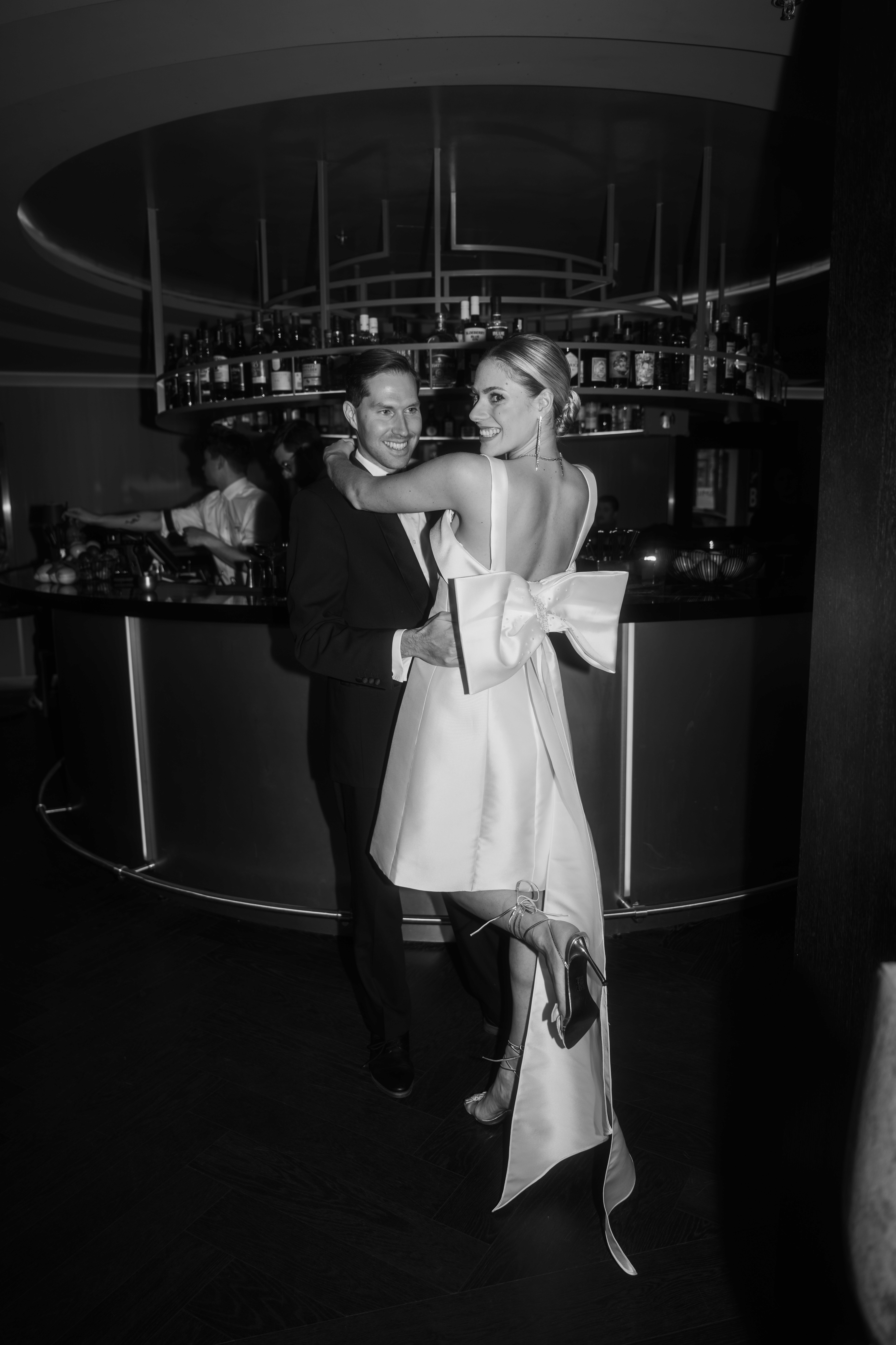 Brautpaar in einer Bar mit kurzem Kleid und einer riesen Schleife am Rücken.
