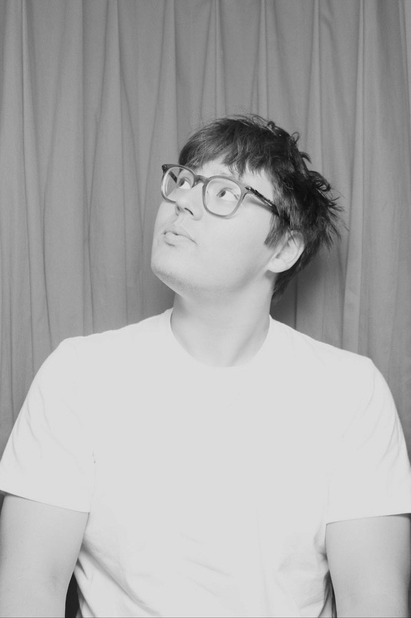 Black and white portrait of a twenty-five year old man wearing glasses looking slightly up to the left.