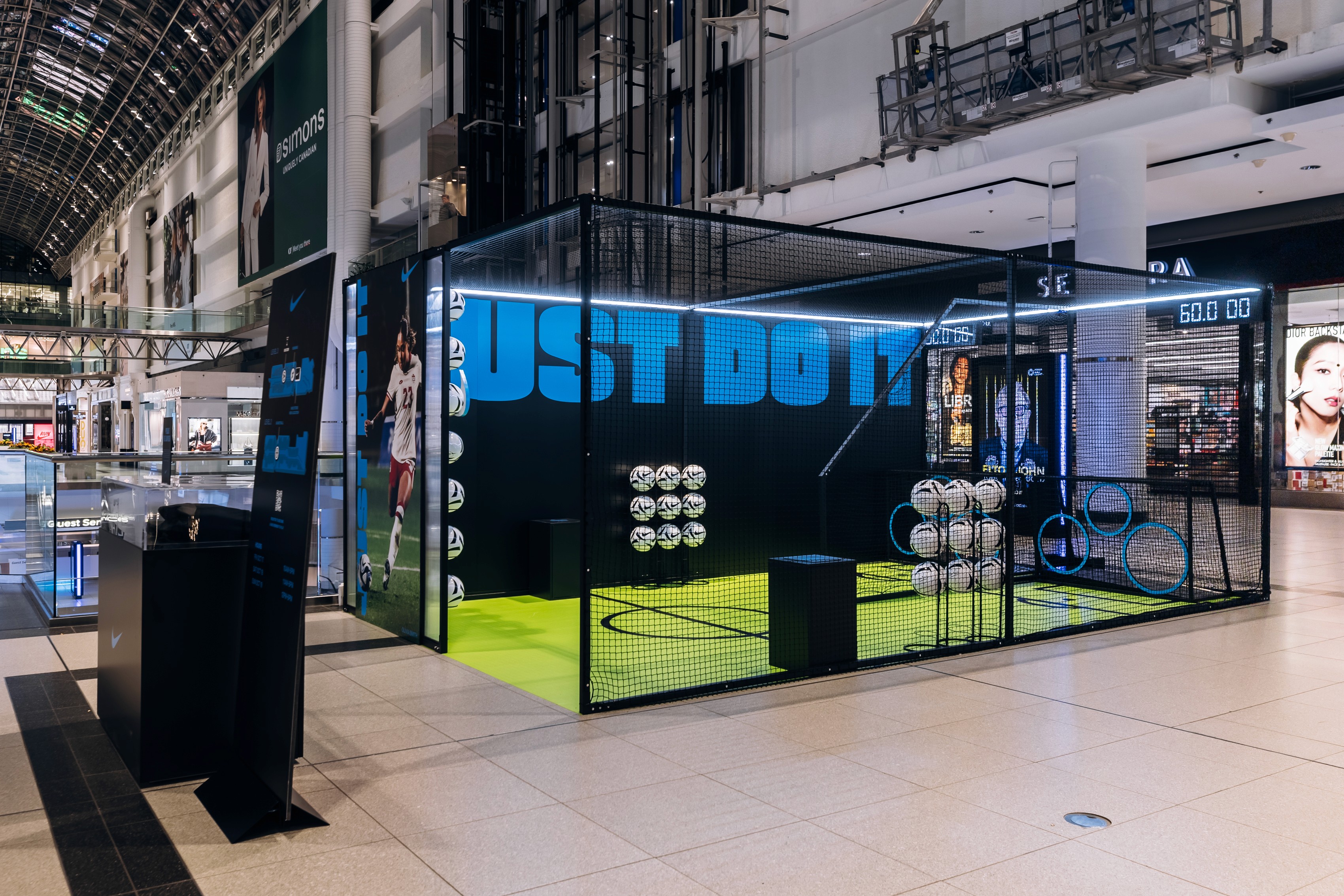 Indoor soccer display at the Eaton Centre featuring a netted area with soccer balls, signage reading "JUST DO IT." Bright, modern lighting and sporty ambiance.