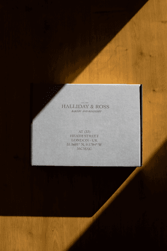 Cardboard box packaging for Halliday and Ross merchandise, on wooden floor with sunlight