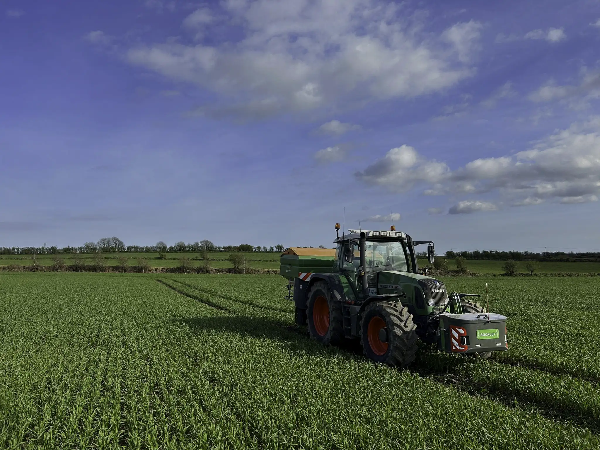 Green Fendt Tractor sitting in a big green field with a grey work box with a custom name plate attached 