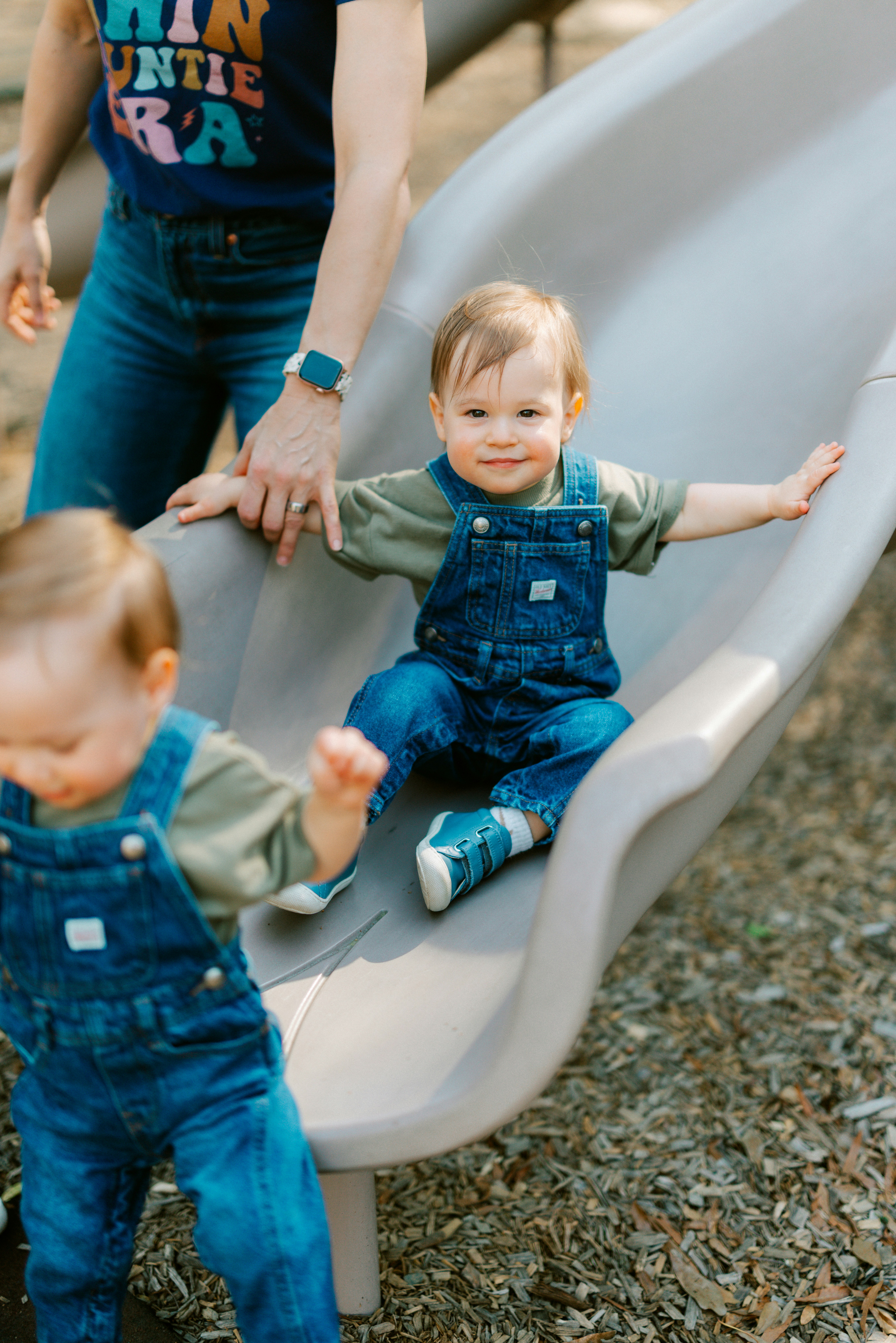 Toddlers in overalls playing on a park slide