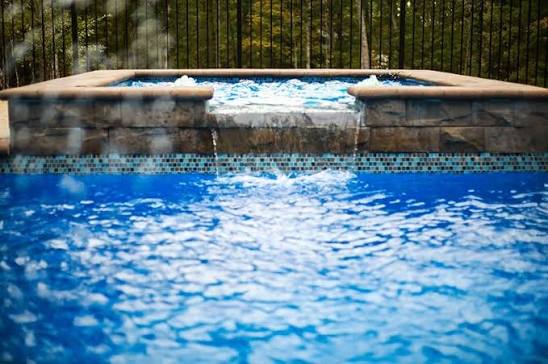 View of professional masonry work for an elevated spa with water overflow, integrated into the design of a residential swimming pool.
