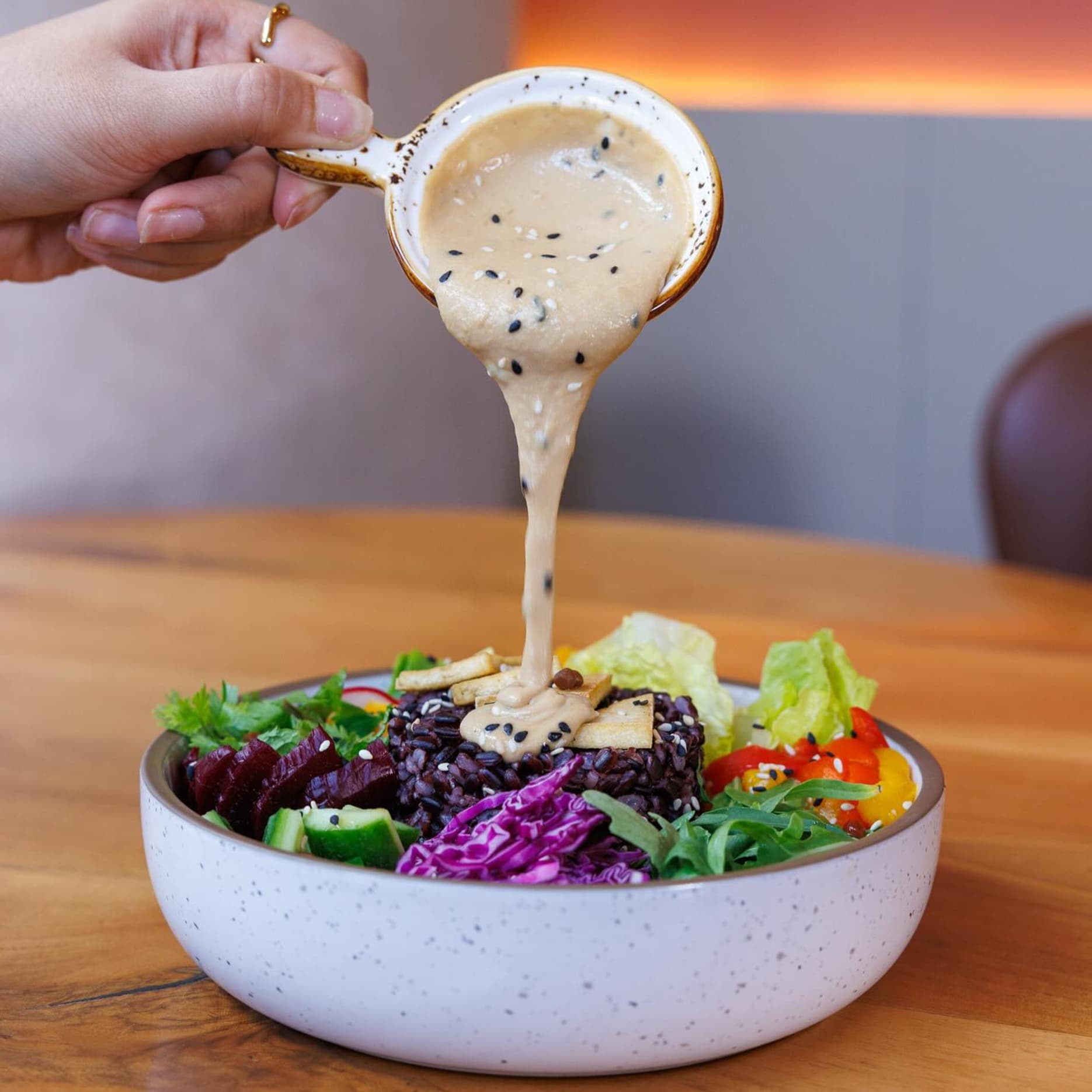 Vegan food, an Ok poke bowl with red rice, roasted vegetables, avocado, pink radish, and smooth tahini dip served fresh and ready.