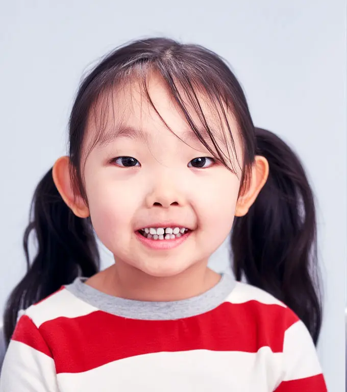 Young Asian girl with pigtails smiling, wearing a red and white striped shirt.