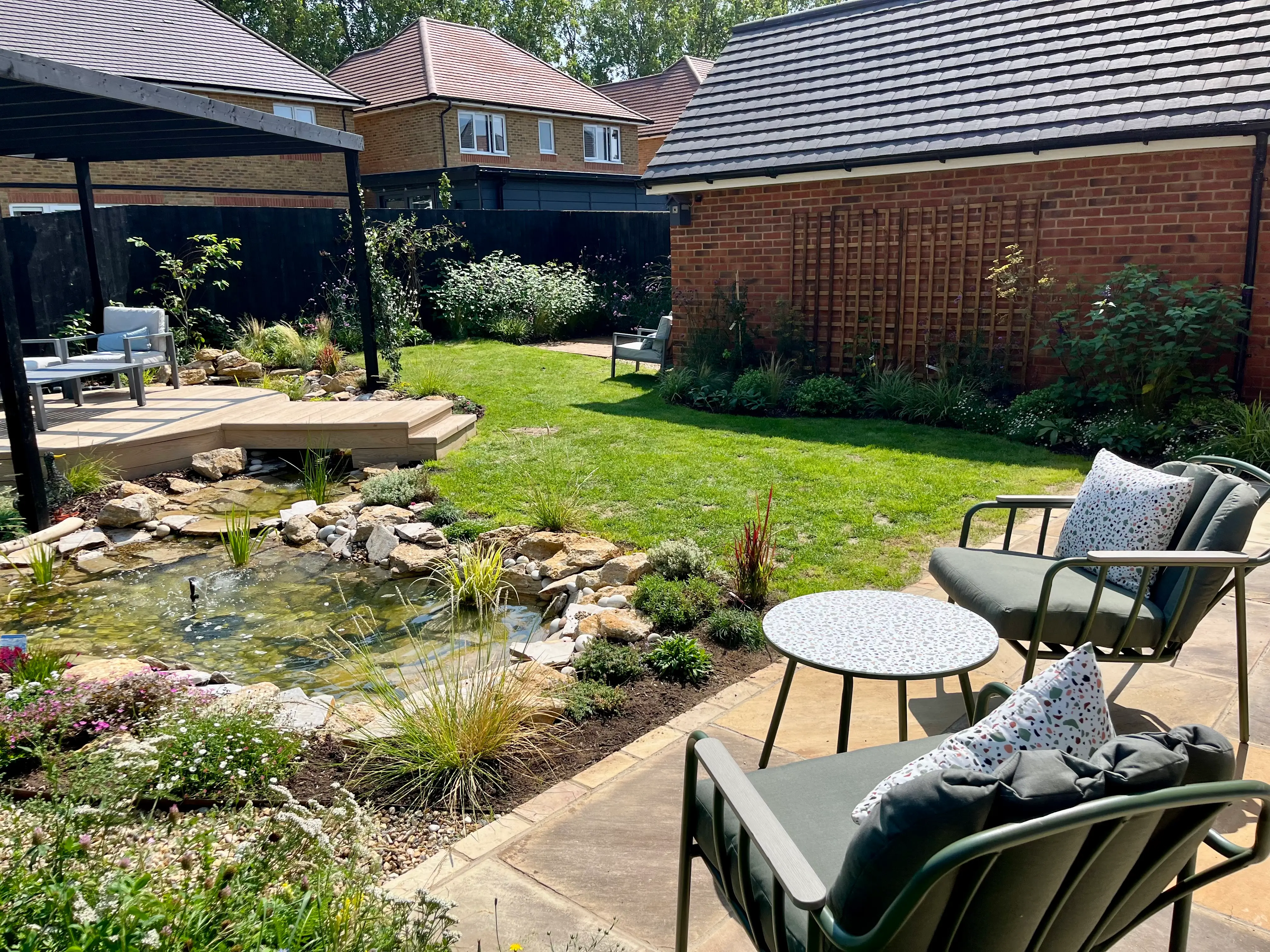 A well-maintained backyard with a garden, pond, and seating area, surrounded by greenery and wooden fences.