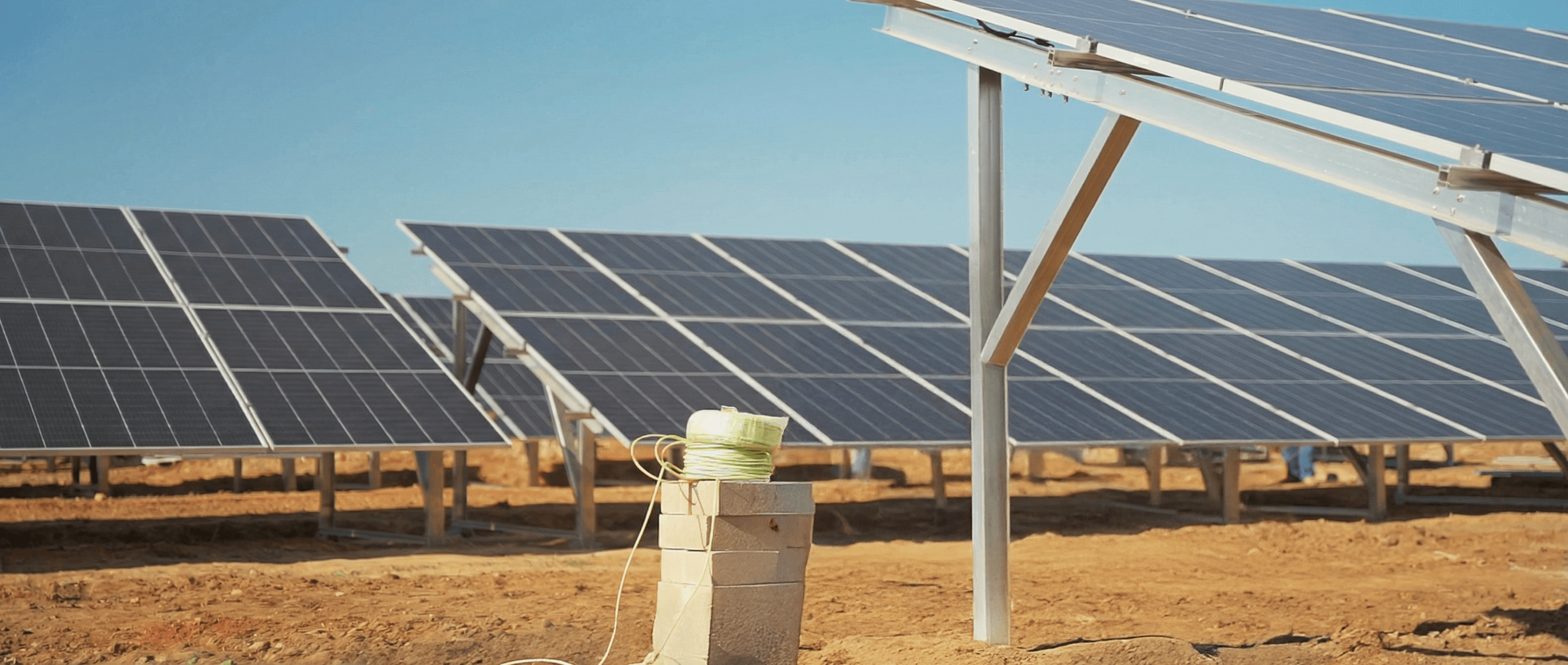 A woman is standing and speaking in a modern conference room with large windows. Two men are seated at a table with laptops, listening intently.