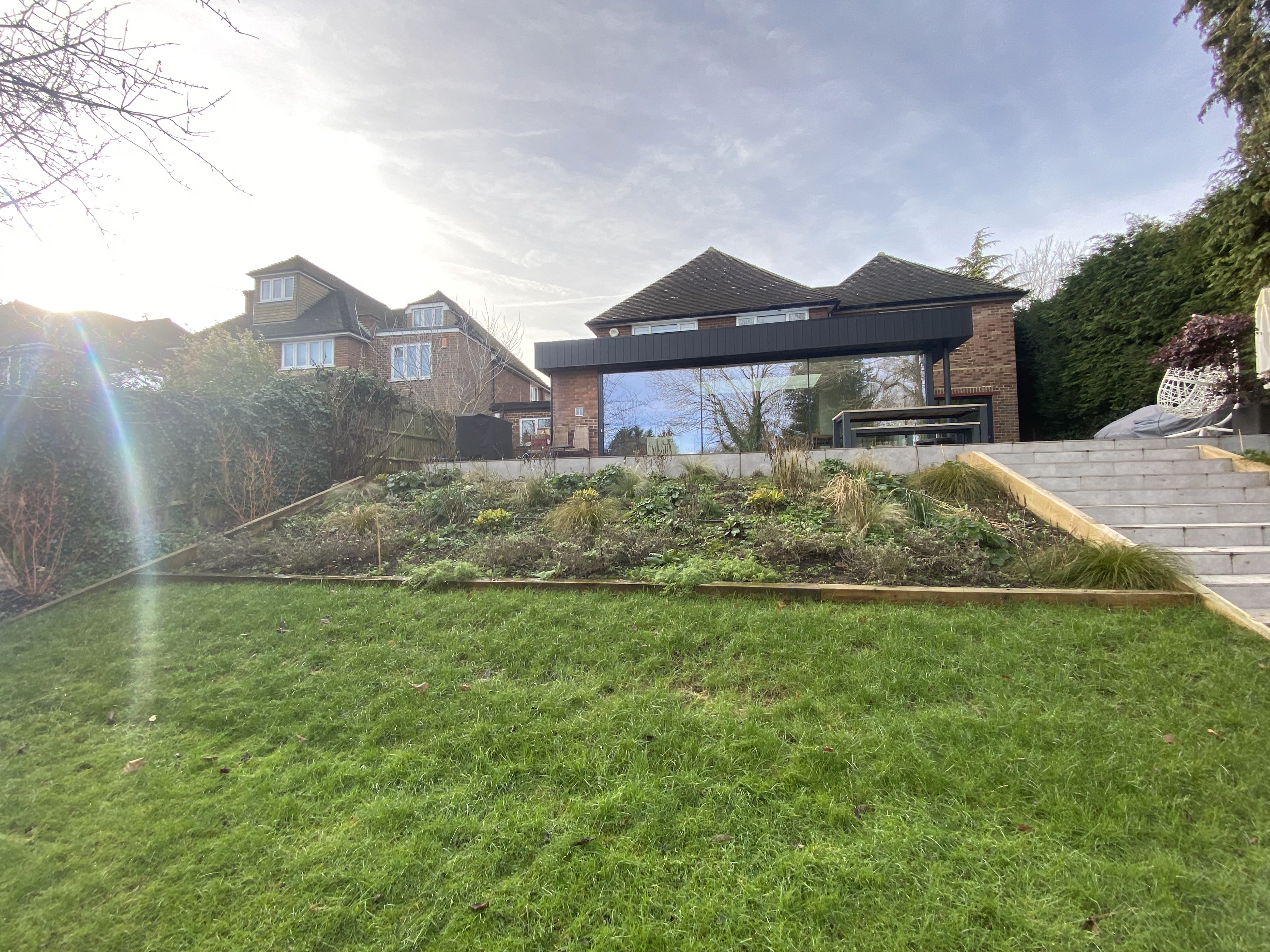 Modern residential house featuring a large glass extension and a multi-level landscaped garden with stone steps and fresh greenery in Chalfont St Peter