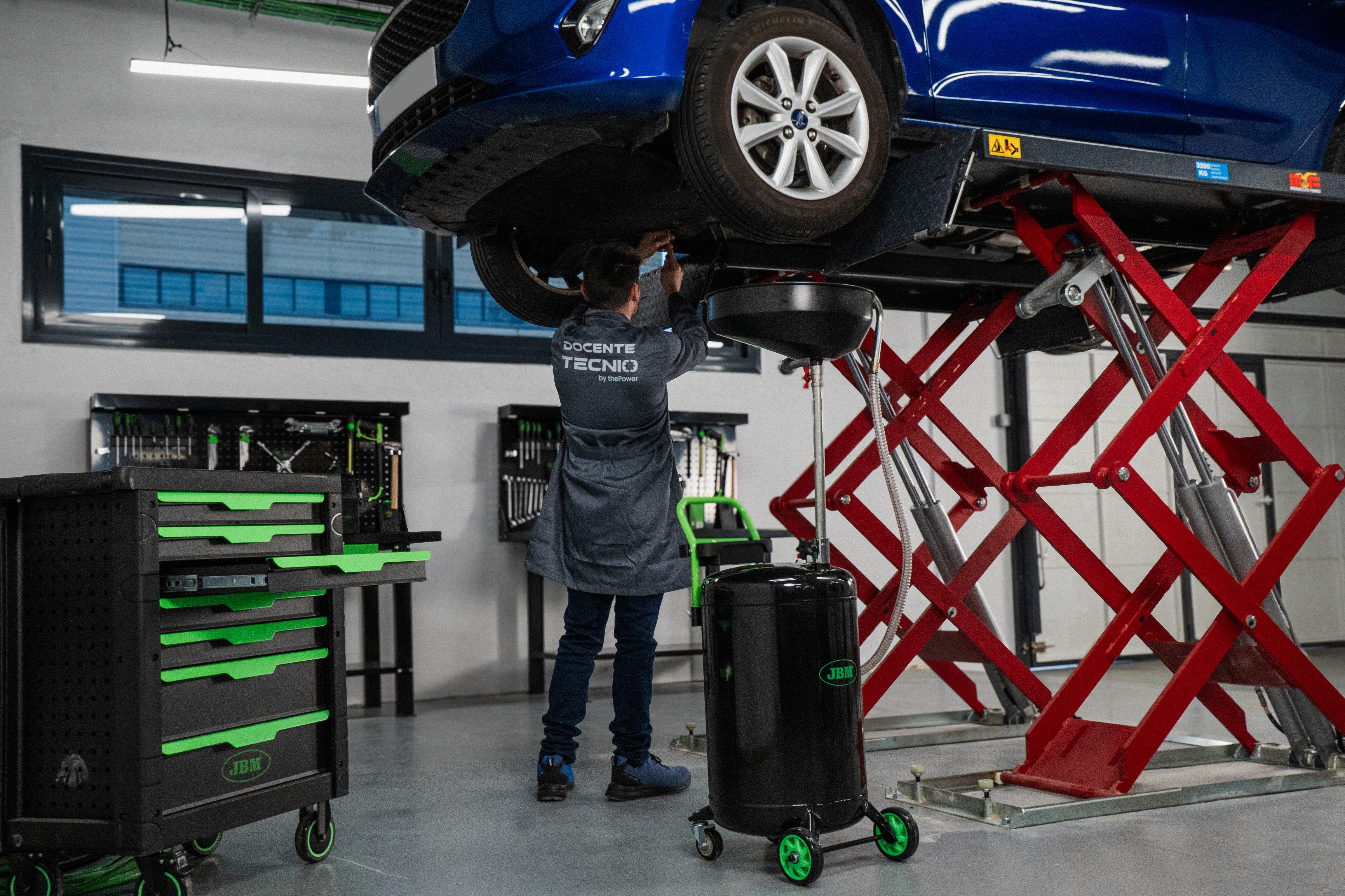 A woman in a teal dress sits in a dimly lit room, focused on her smartphone. A laptop and notepad are on the glass table, suggesting a working environment.