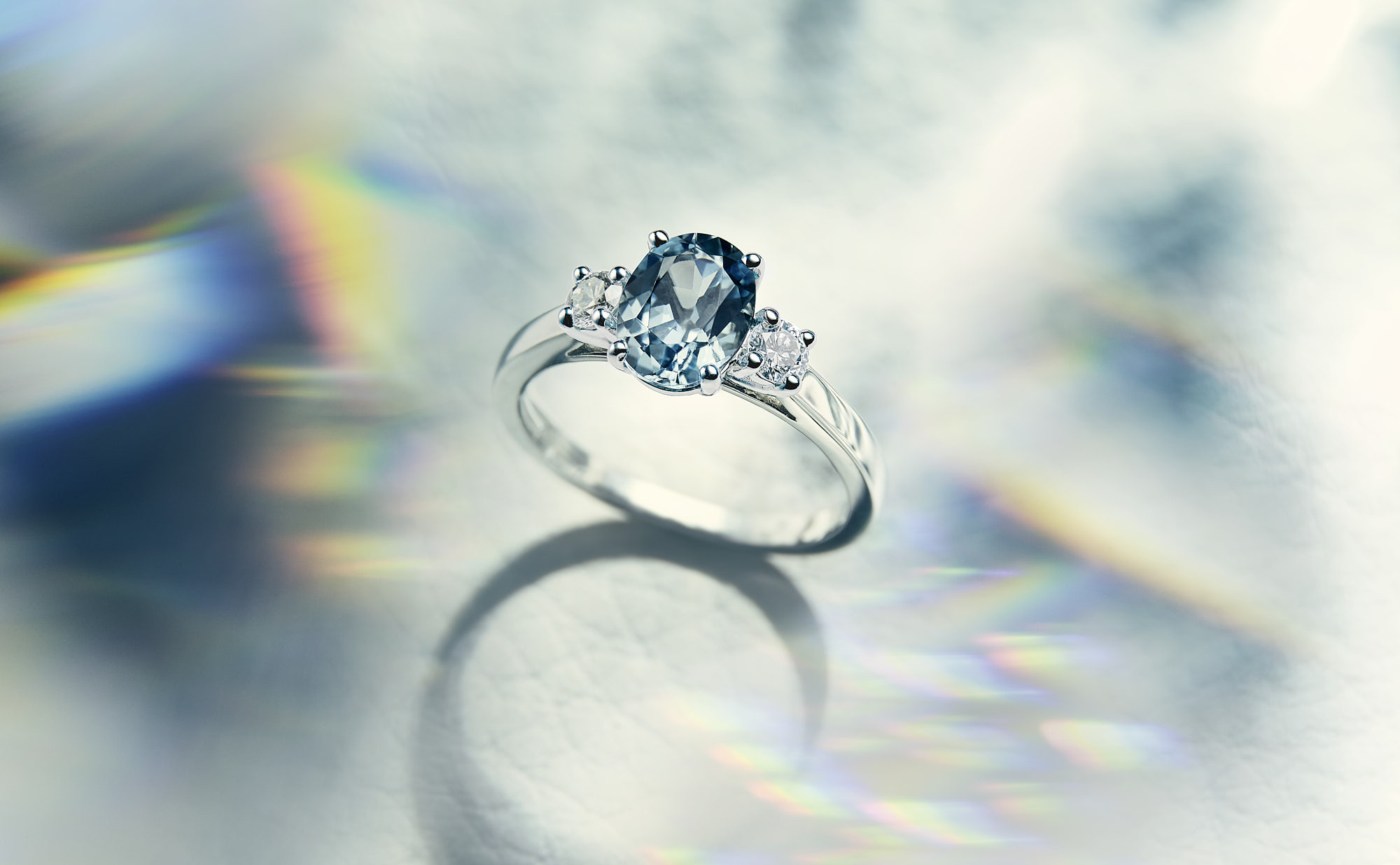 Elegant ring with an oval blue gemstone and diamond accents on a reflective surface.