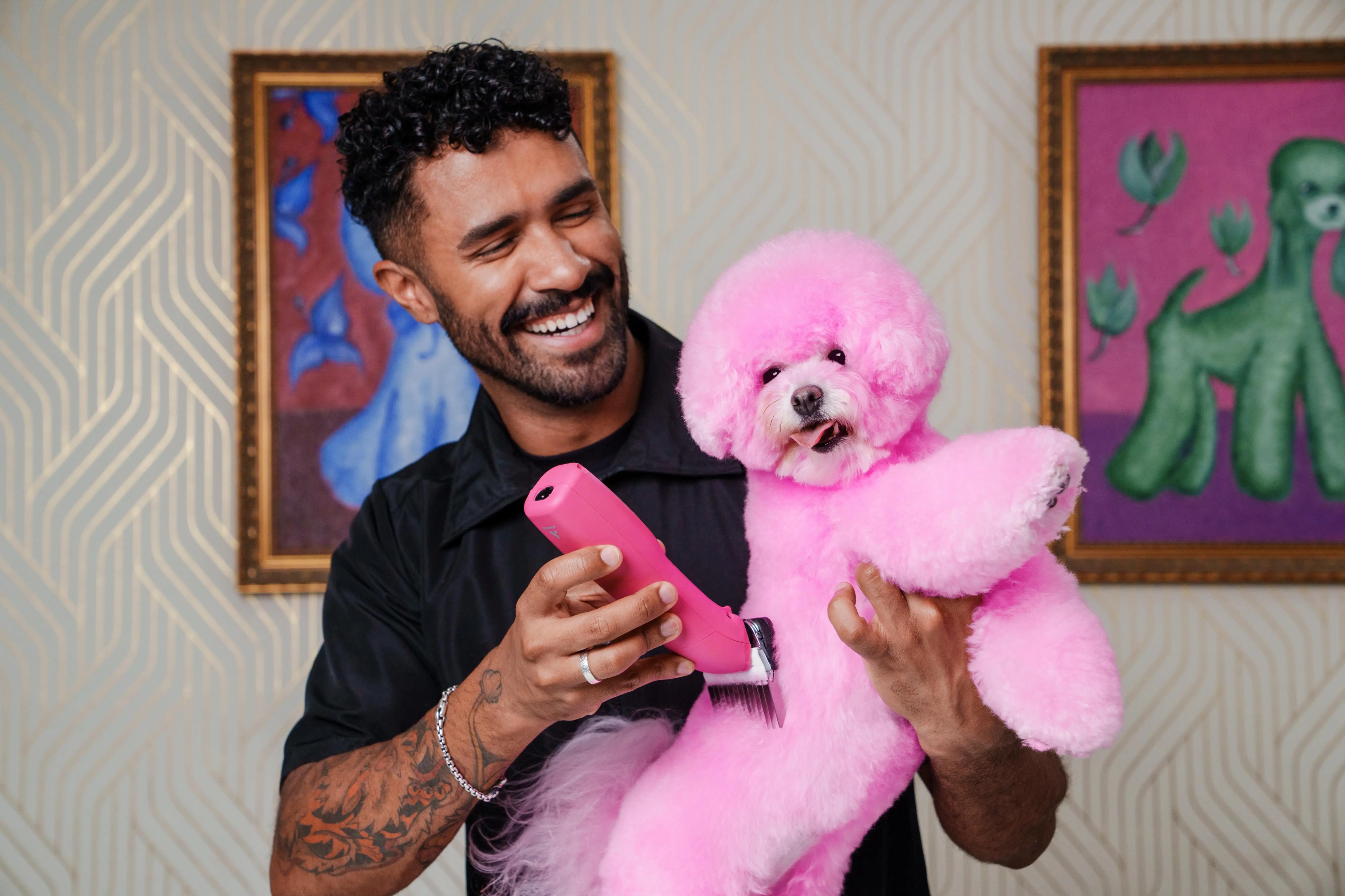Two groomers styling a white poodle with colorful creative grooming designs in a neon-lit studio, featuring pastel purple and yellow accents