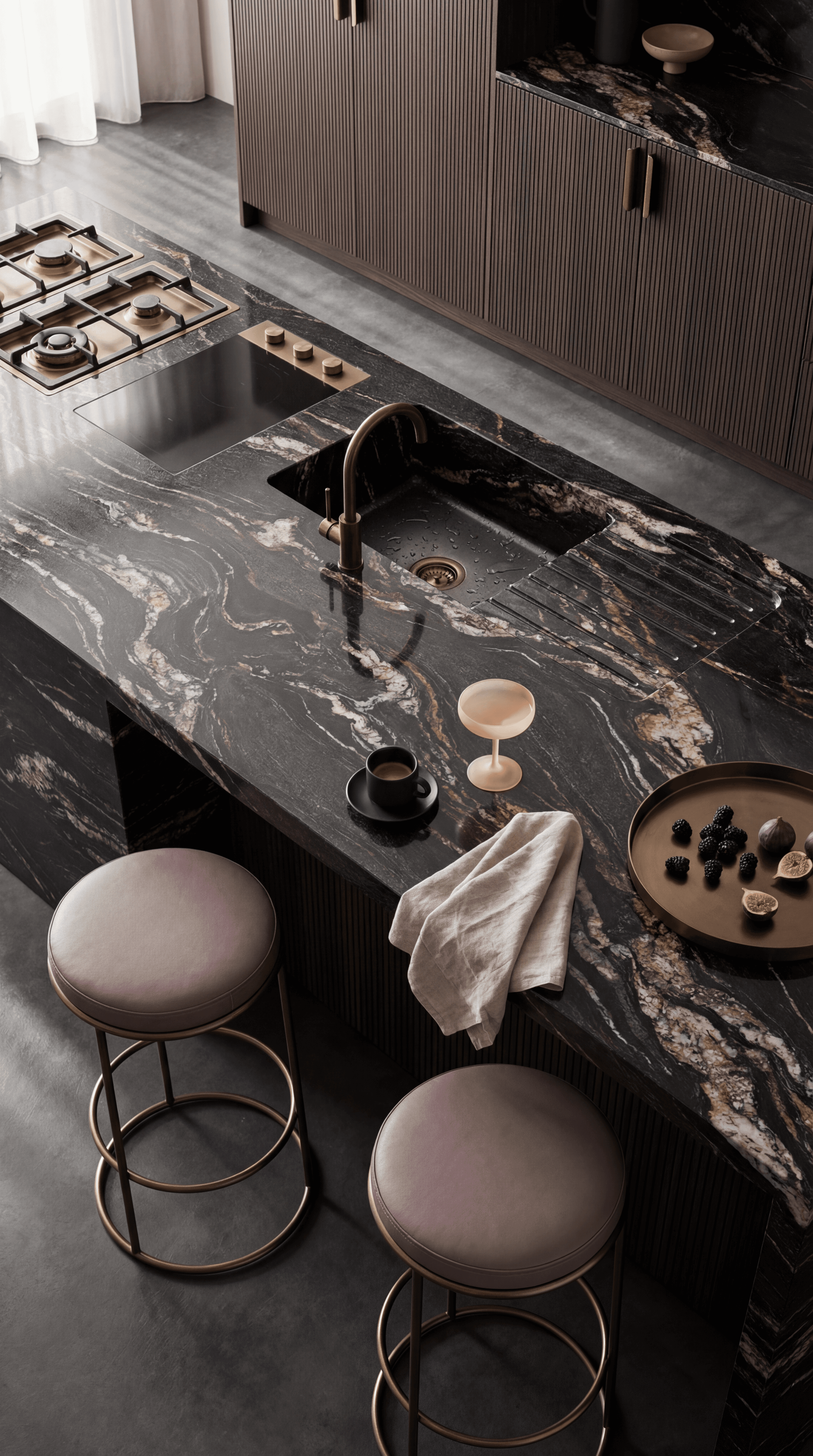 High-end kitchen island in dark granite with integrated sink, cooktop and styled accessories, editorial angled view