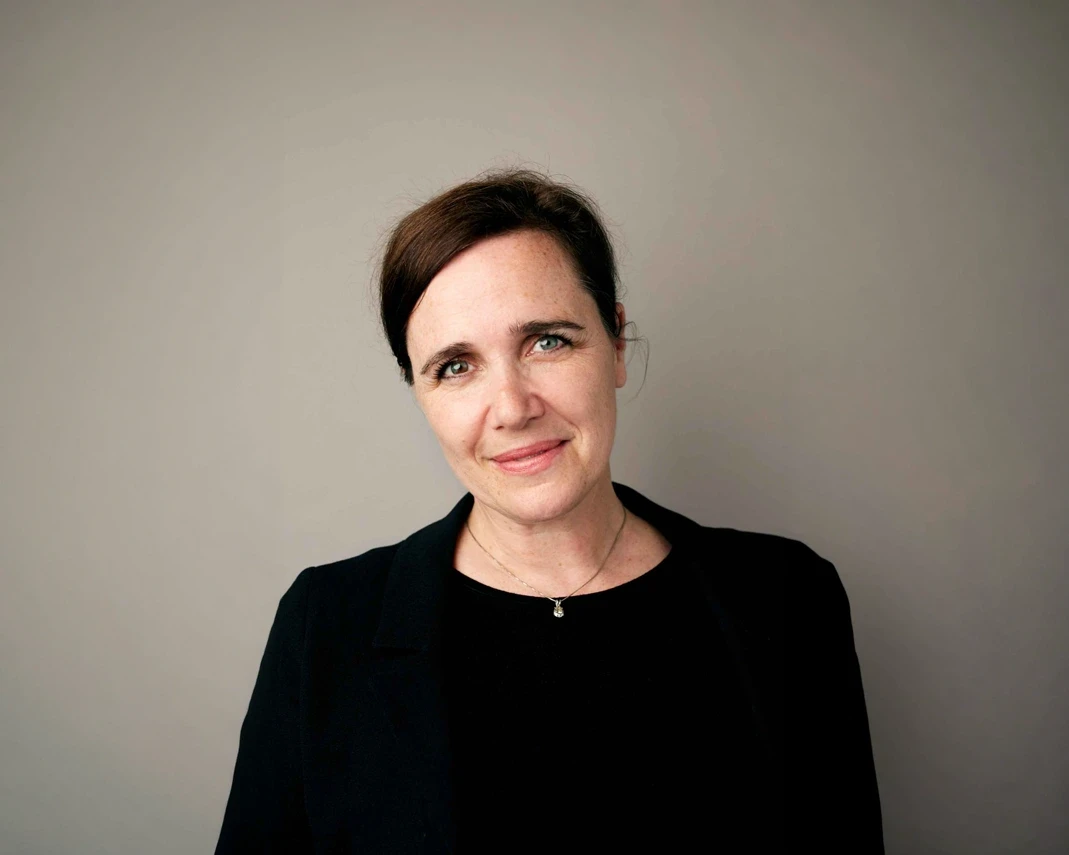 Woman in black blazer and necklace, grey background