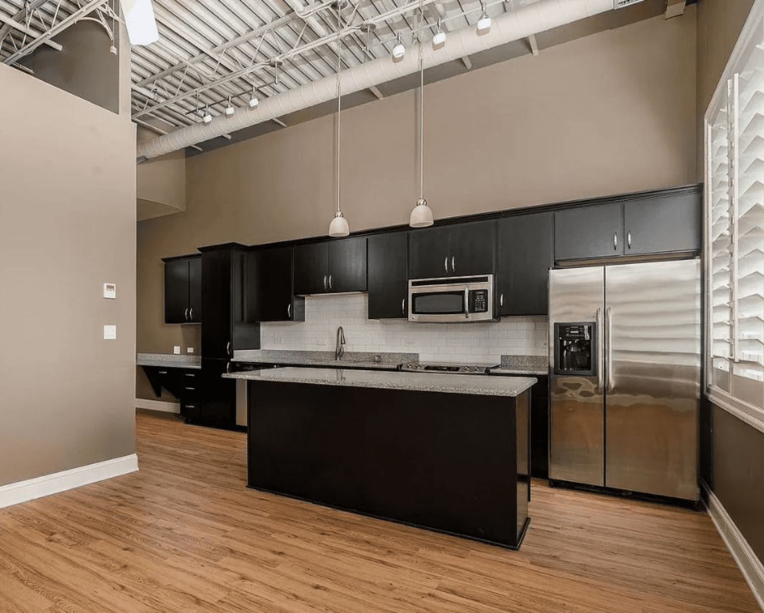 Modern industrial-style kitchen at The Gateway Village apartments for rent, featuring dark wood cabinets, granite counters, and high ceilings for a spacious, comfortable feel.