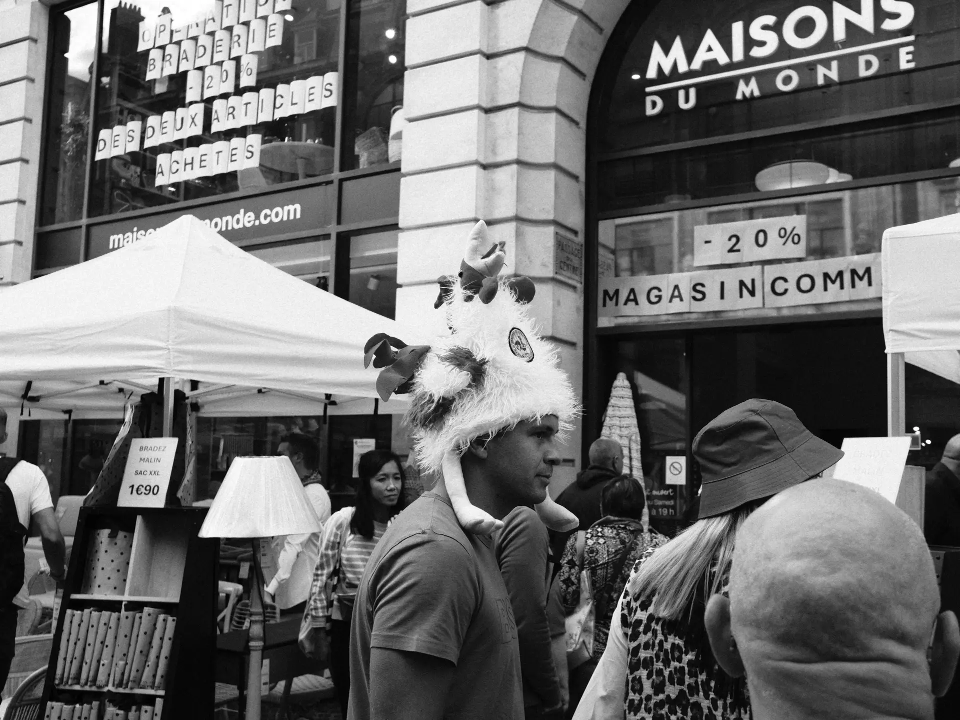 Market stalls and shoppers outside a store, in black and white