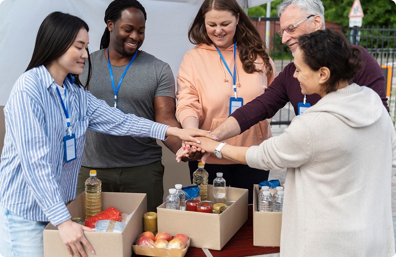 Group of diverse volunteers putting their hands together in unity over donation boxes