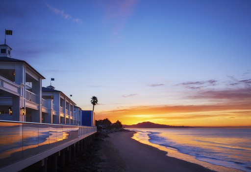 A serene seaside view at sunset, with a high-end and luxurious stay, walkway beside gentle waves and a colorful sky .