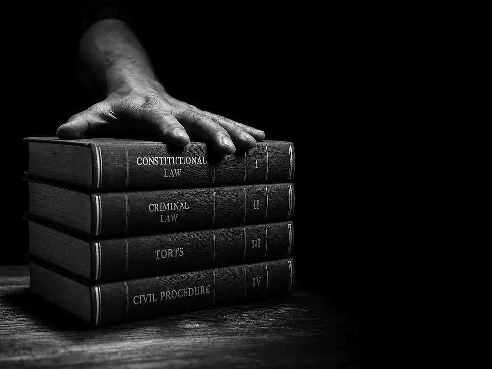 Main posée sur une pile de codes juridiques, fond noir contrasté.