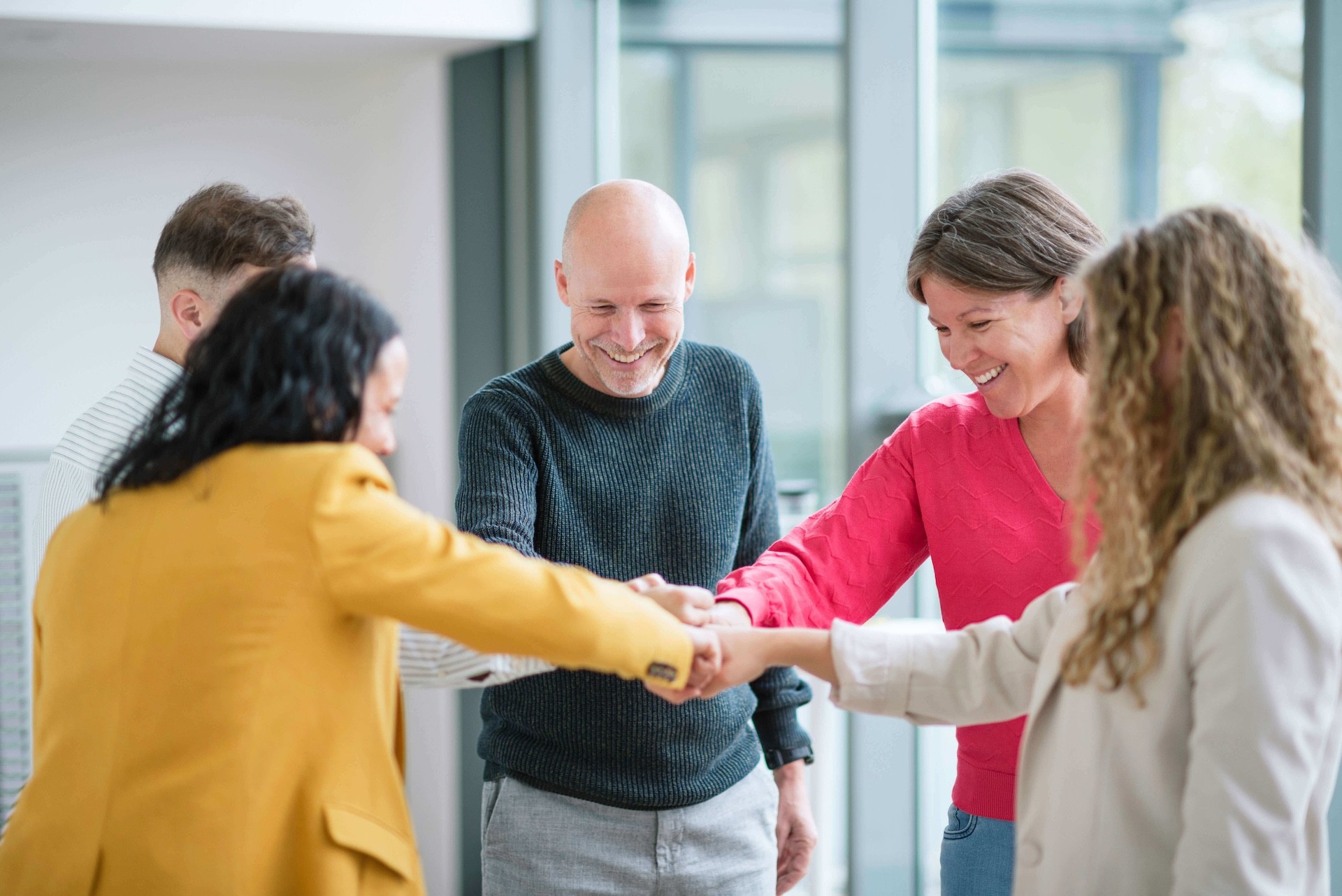 Team members celebrating success together, smiling and joining hands as a symbol of winning together.