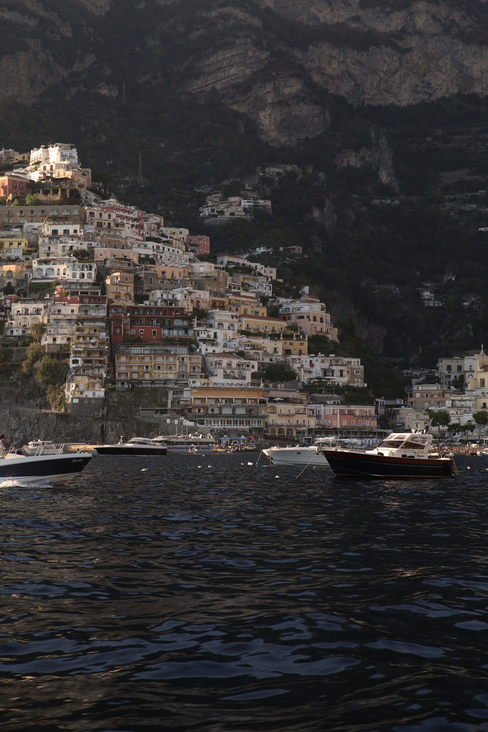 Boats moored in a harbour beneath a cliffside town of colourful buildings