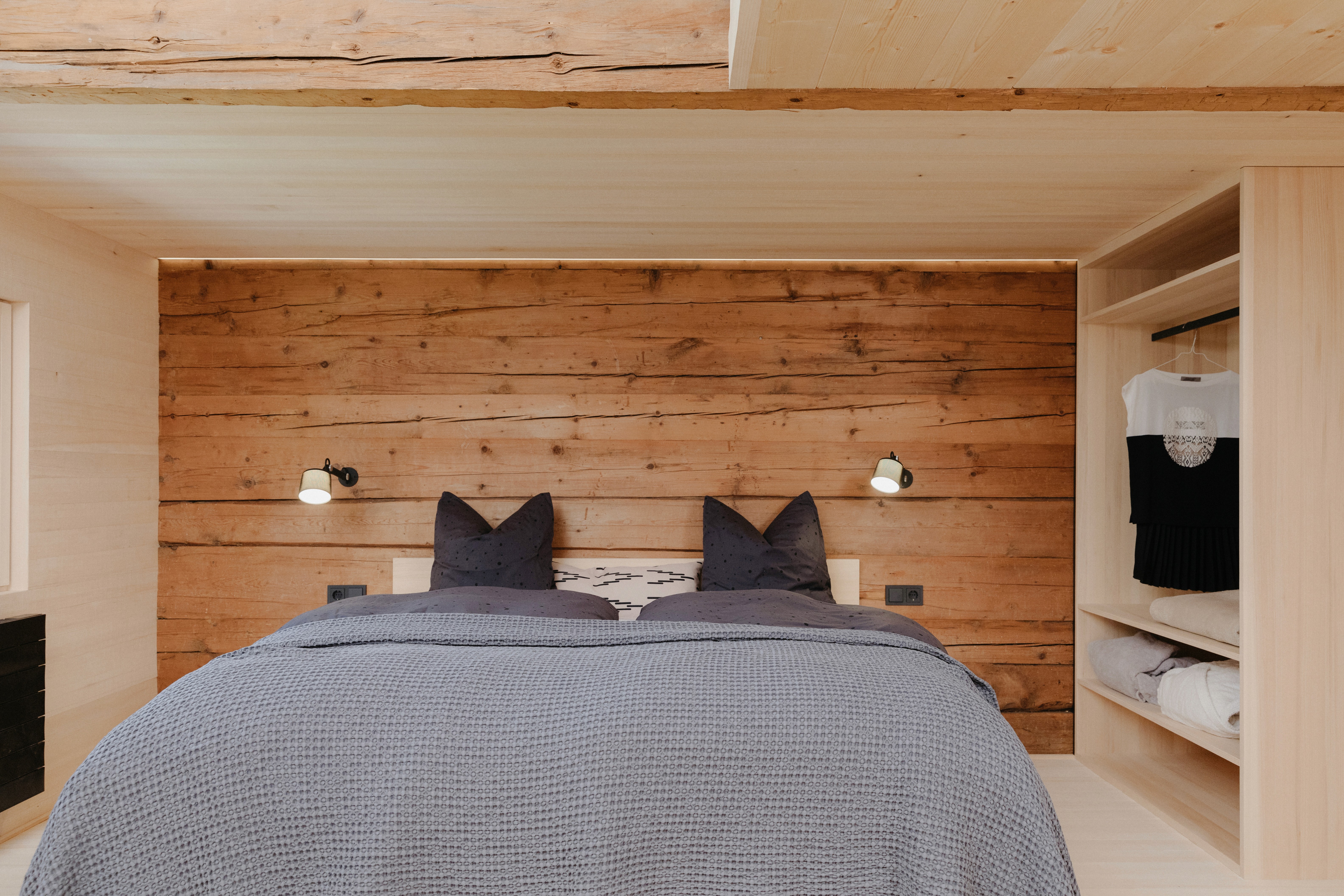 A bed covered by a grey overthrow in a wooden bedroom.