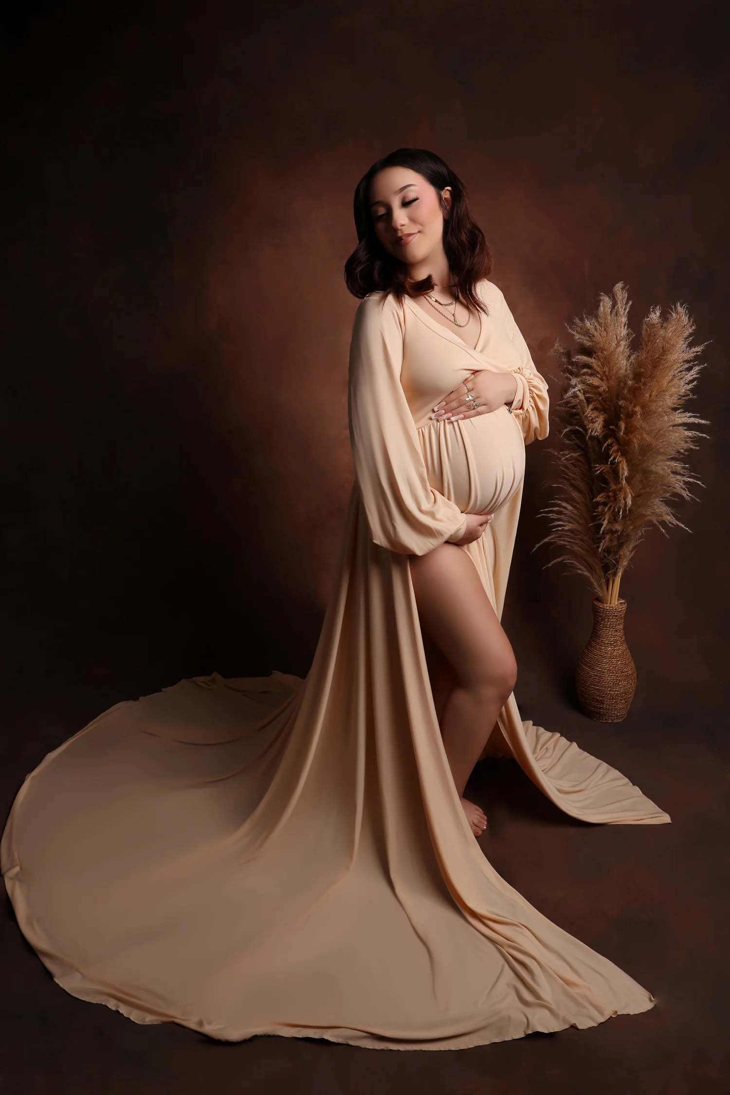 Woman in a flowing tan gown standing by dried florals