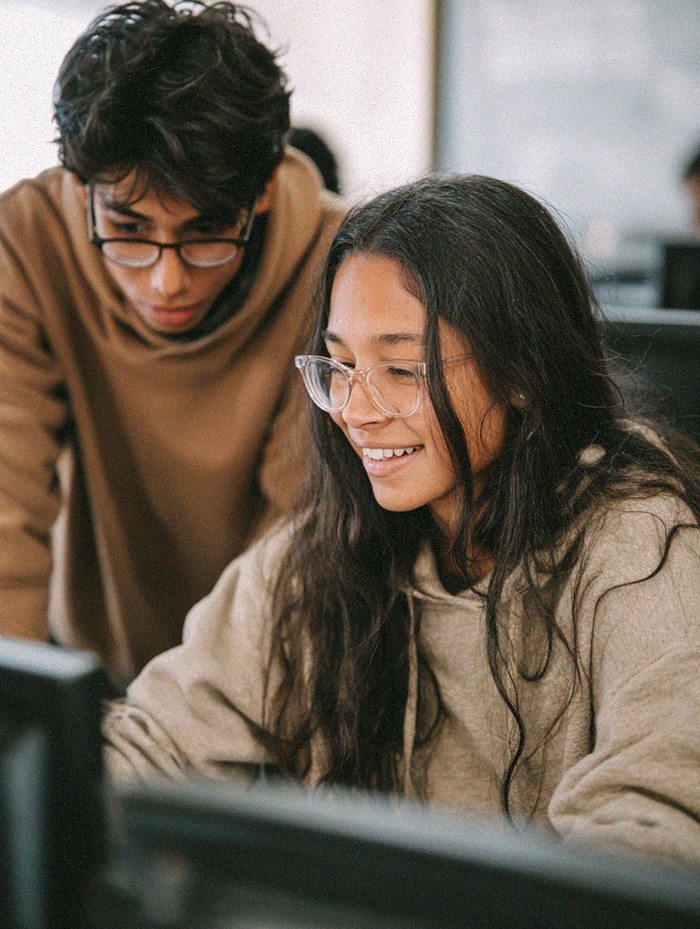 Two students working together at a computer, collaborating on a project in a classroom or lab.