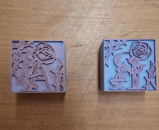 3D printed dropcaps for the letters A and R. Both designs feature roses on the letterforms and thorns in the corners of the designs.