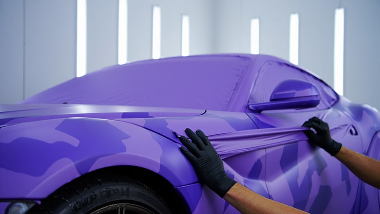 Photo de main en train d'appliquer un vinyl covering sur la carrossserie d'une voiture