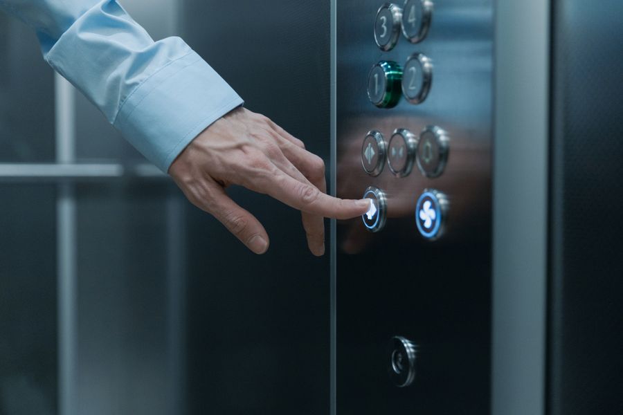 A hand pressing a button on a modern elevator control panel