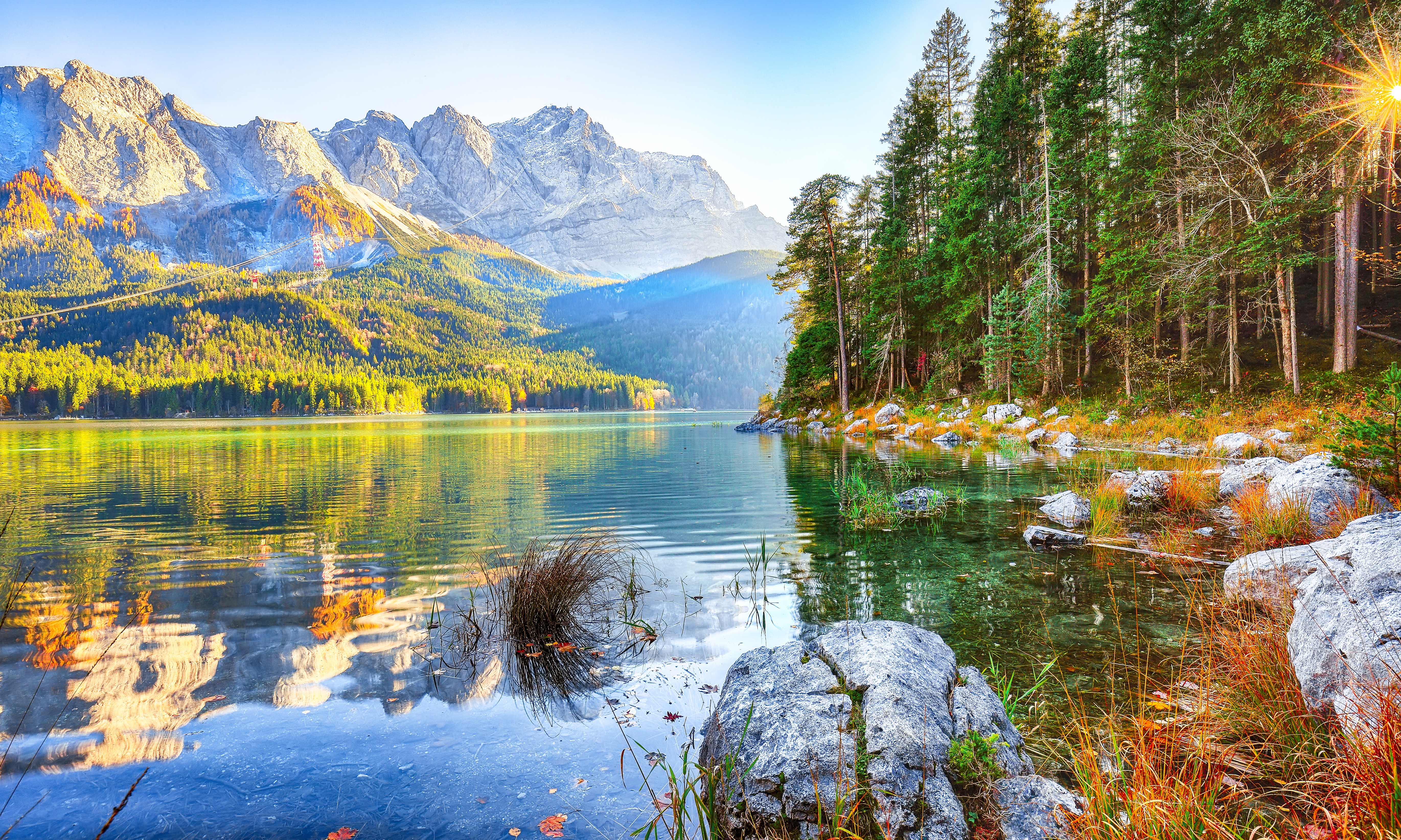 An alpine lake against a mountain backdrop, with warm autumn colors and trees along the shore.