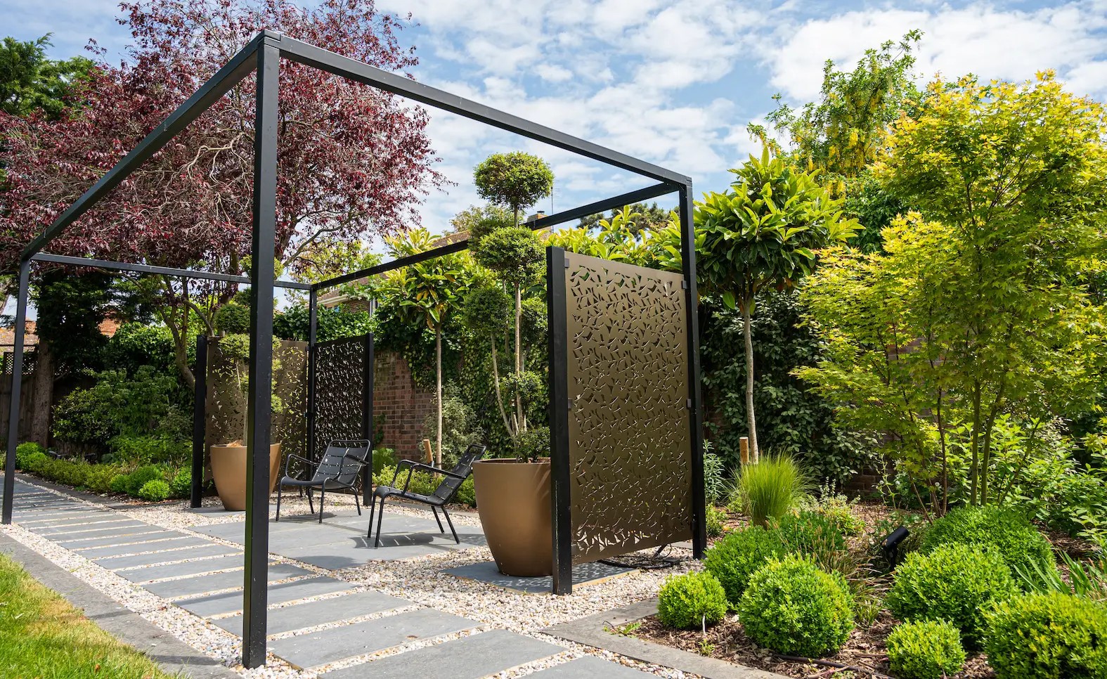 A modern garden entrance features a metal frame and lush greenery, creating a serene outdoor space.