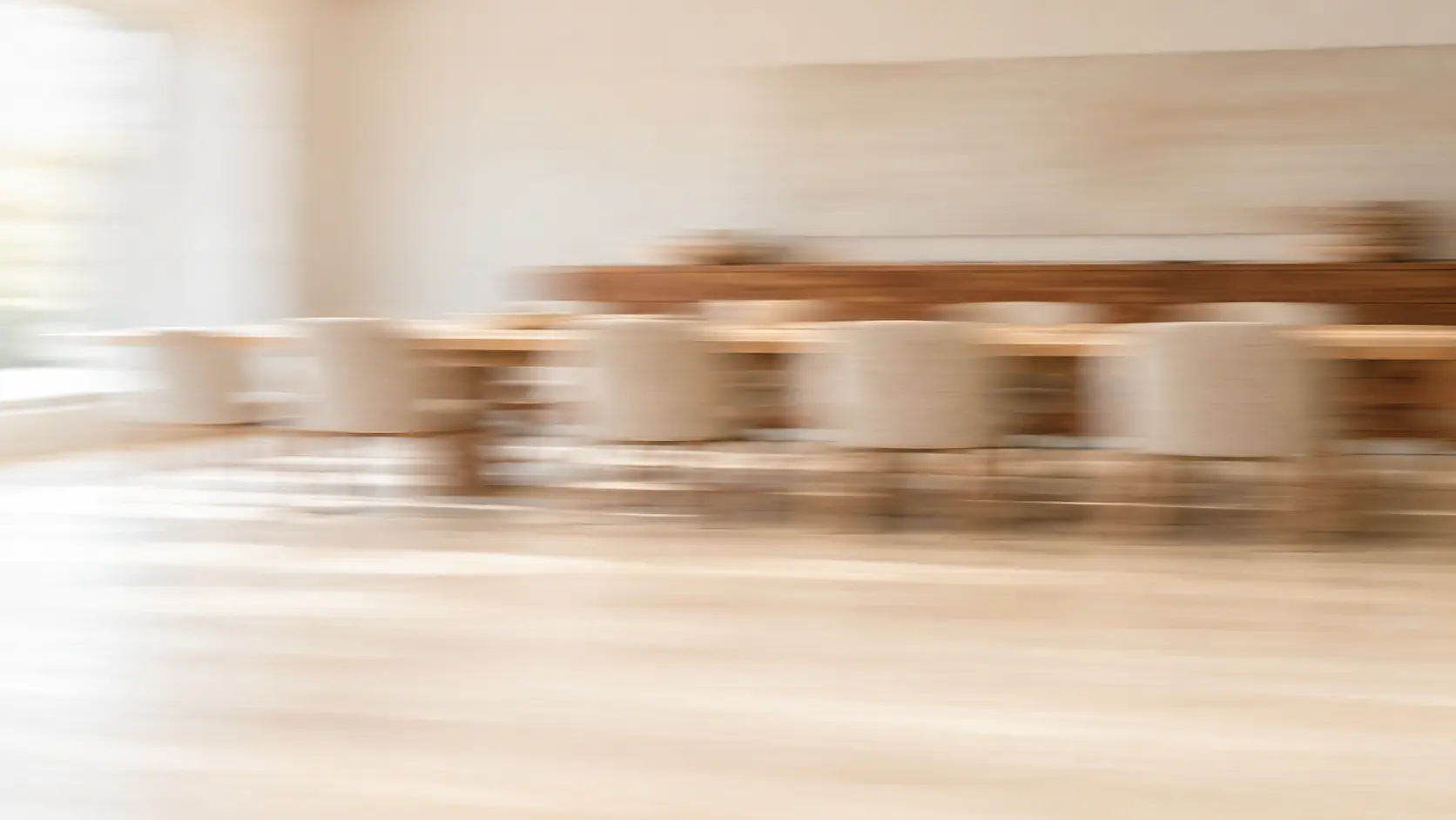 Daylit meeting room with a long oak table, softly blurred by motion