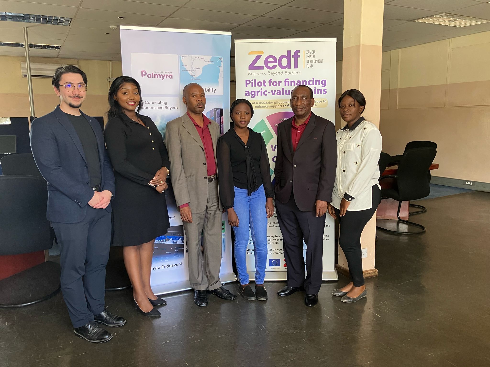 A person sits at a cluttered desk in a dimly lit room, focused on two monitors displaying aerial maps. The walls are covered with various images and notes.