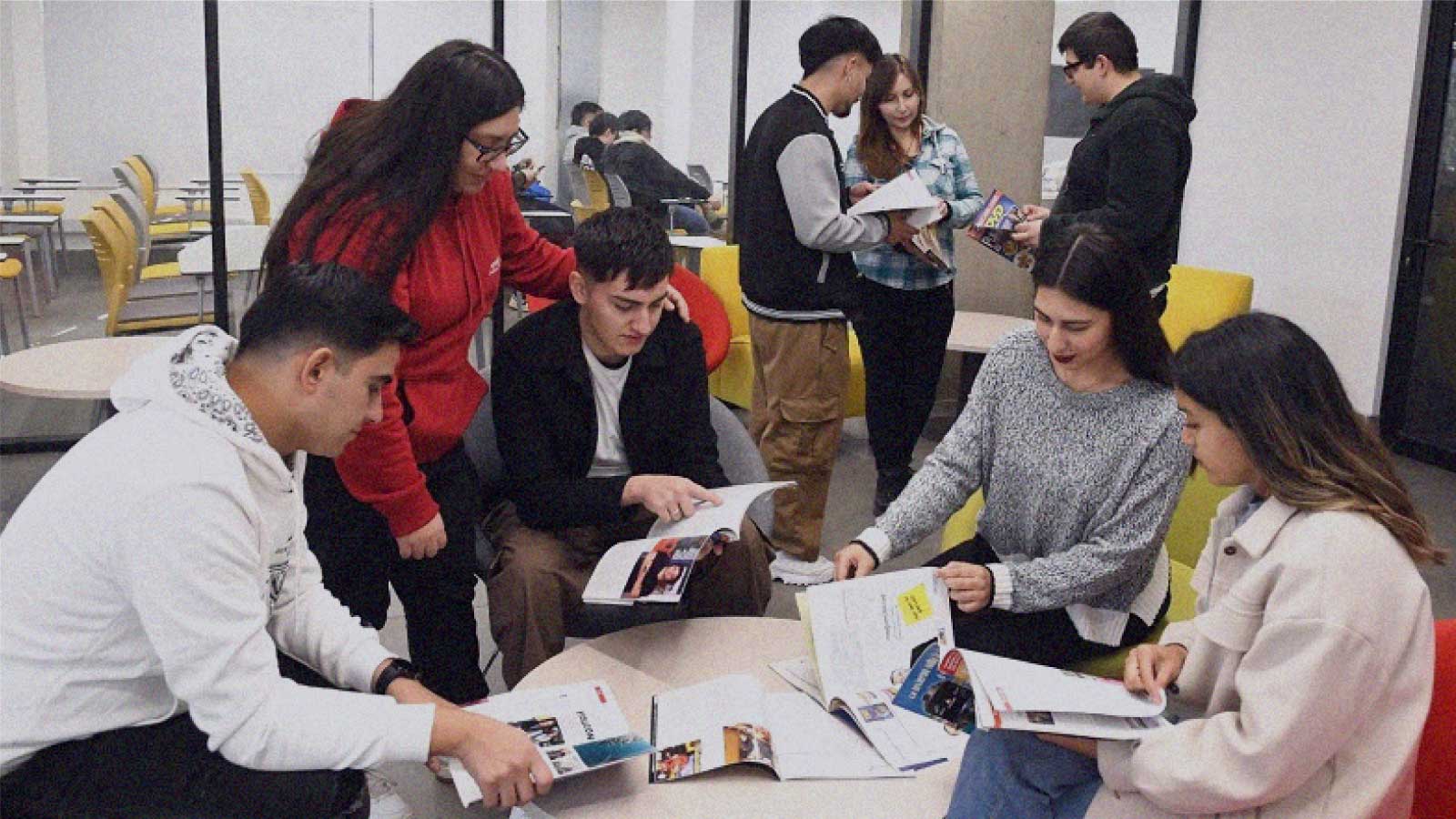 Imagen de cinco jóvenes alrededor de una mesa mientras hojean revistas en la columna de opinión Cruzando datos de IdeaPaís.